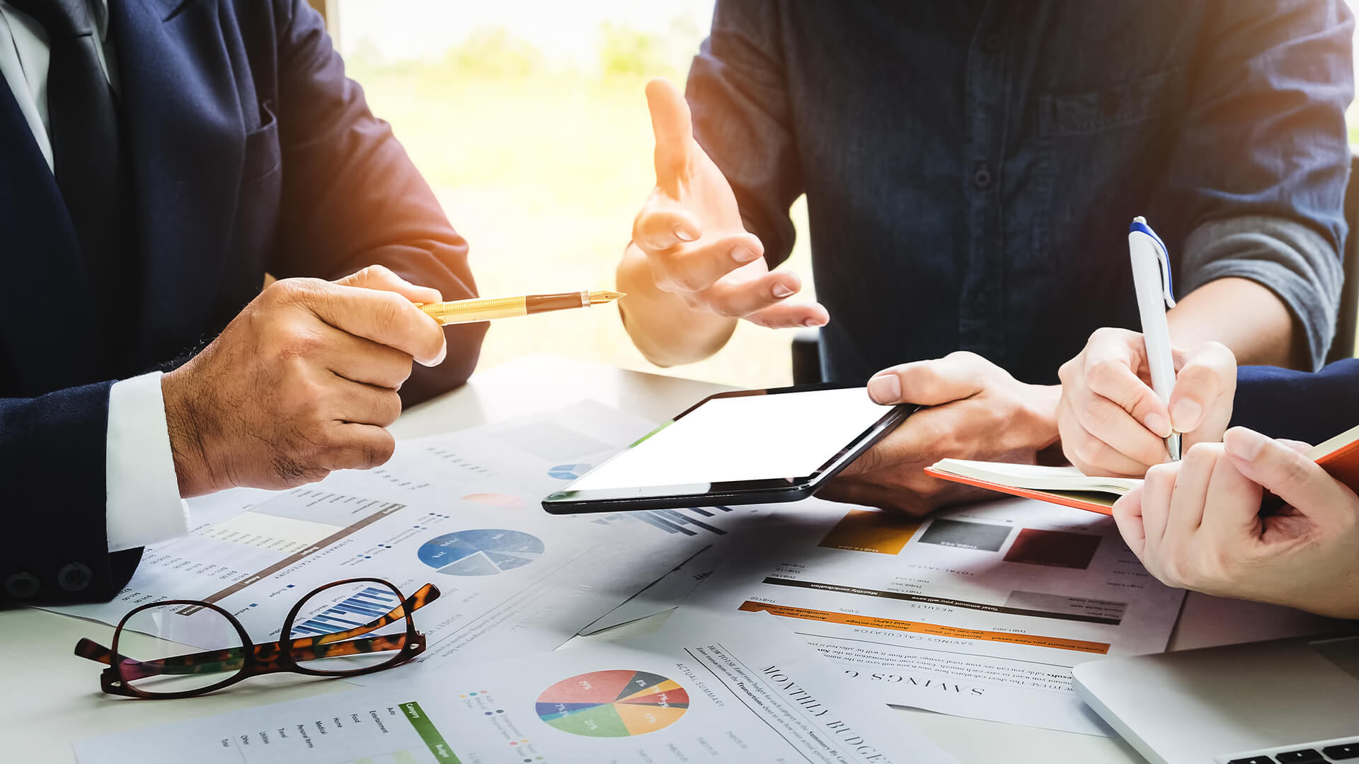 Three people having a business meeting about their finances, with papers and graphs scattered on the table