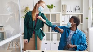 Two office workers wearing masks and bumping elbows