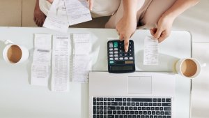 Two people using a calculator and laptop to do online bookkeeping