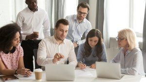 Office employees gathered around computers to recieve training from a sernior memeber of staff