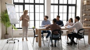 Smiling mature 60 year old businesswoman flip charts presentation new project in boardroom at company meeting.