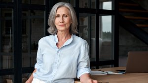 Confident older CEO, business woman standing slouched in front of a desk