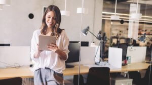 CEO standing in front of a table, holding a tablet, looking down at it while smiling