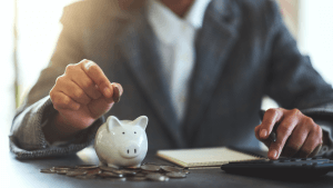 Closeup image of a woman putting coins in a piggy bank and calculating with calculator