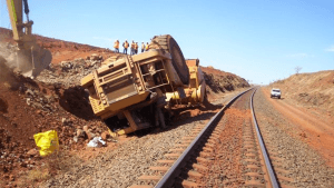 Workers working outside in a desert by train tracks lifting a rolled over vehicle