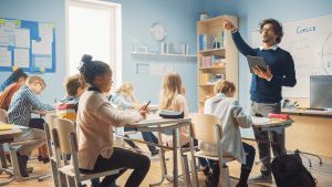 Enthusiastic Teacher Giving a Lesson in Elementary School to Class Full of of Diverse Children