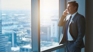 Mature business CEO talking on phone alongside large high windows