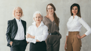 Successful business women. Well educated female leaders. Young and mature ladies standing together confidently over light wall.