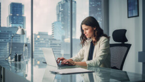 Portrait of Young Successful Caucasian Businesswoman Sitting at Desk Working on Laptop Computer in City Office.