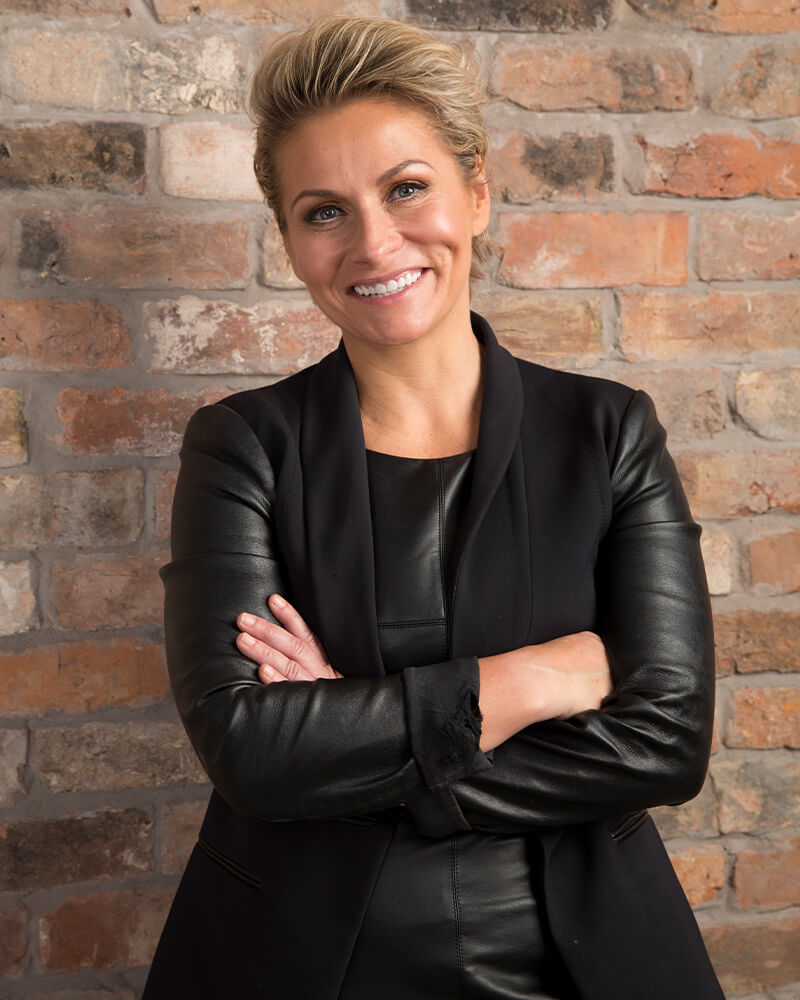 CEO standing in front of brick wall with hands crossed and smiling