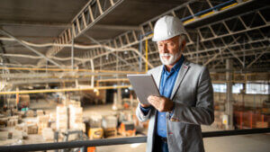 Factory CEO or manager in business suit and hardhat standing in production hall and checking results of his company.