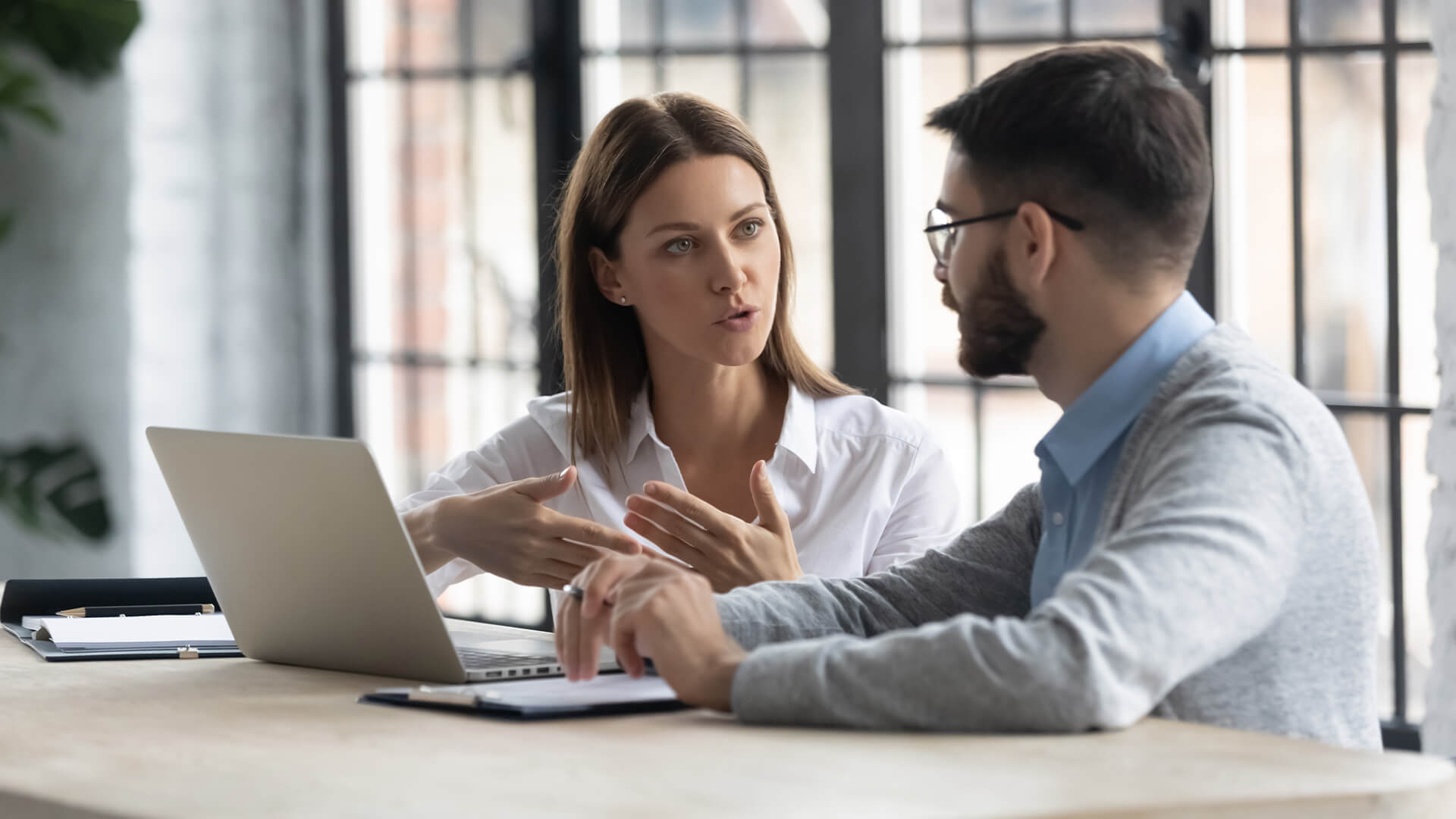 Concentrated diverse businesspeople sit at desk talk brainstorm at office meeting using laptop