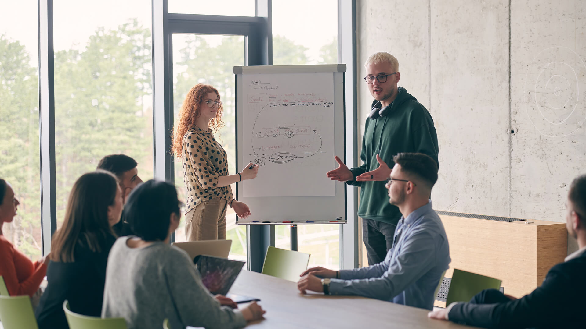 In a modern office setting, a group of business professionals attentively listens to a captivating presentation delivered by their young colleagues, showcasing their teamwork