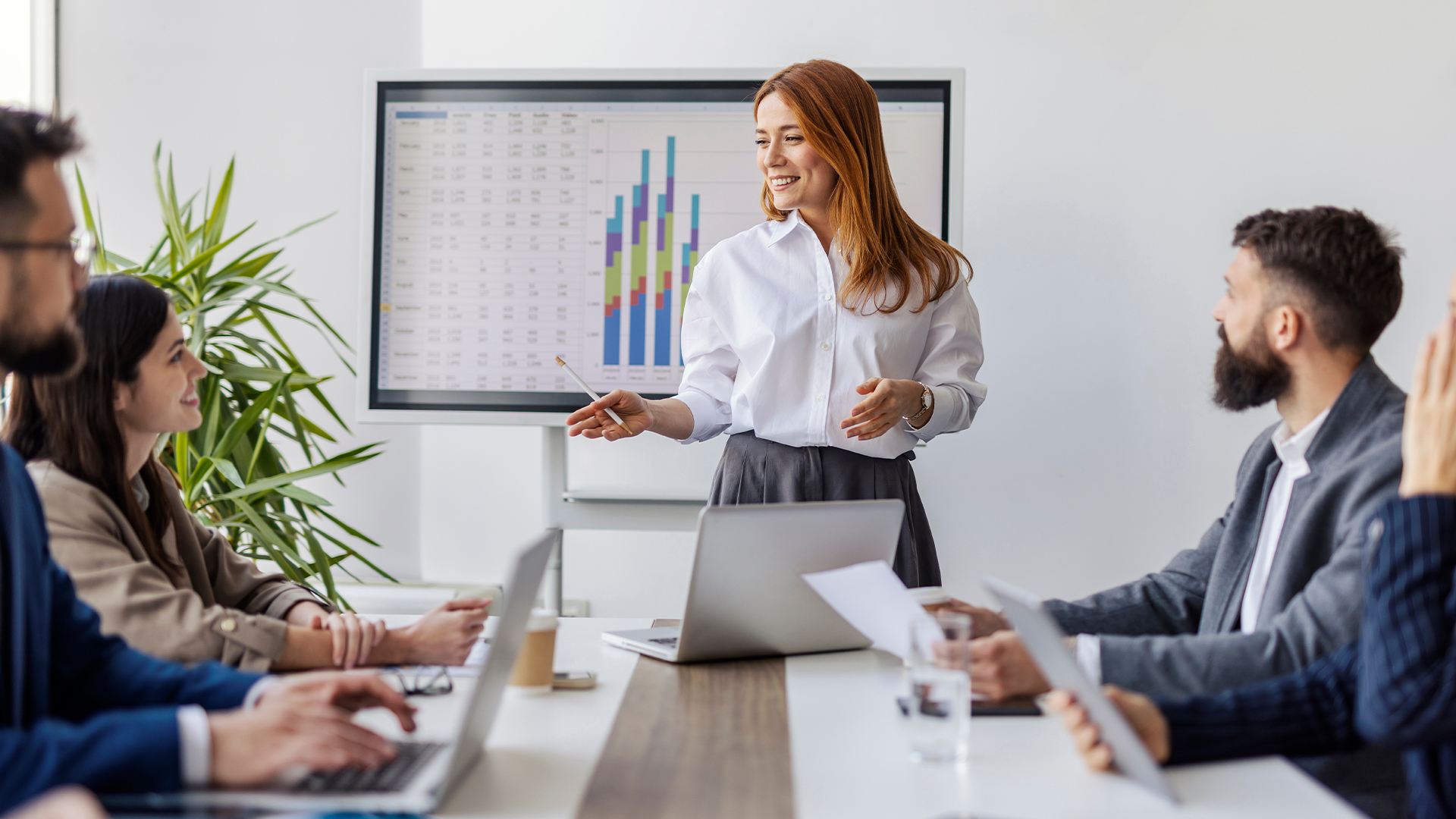 Portrait of female executive standing near conference table at boardroom with her leadership team and explaining financial report