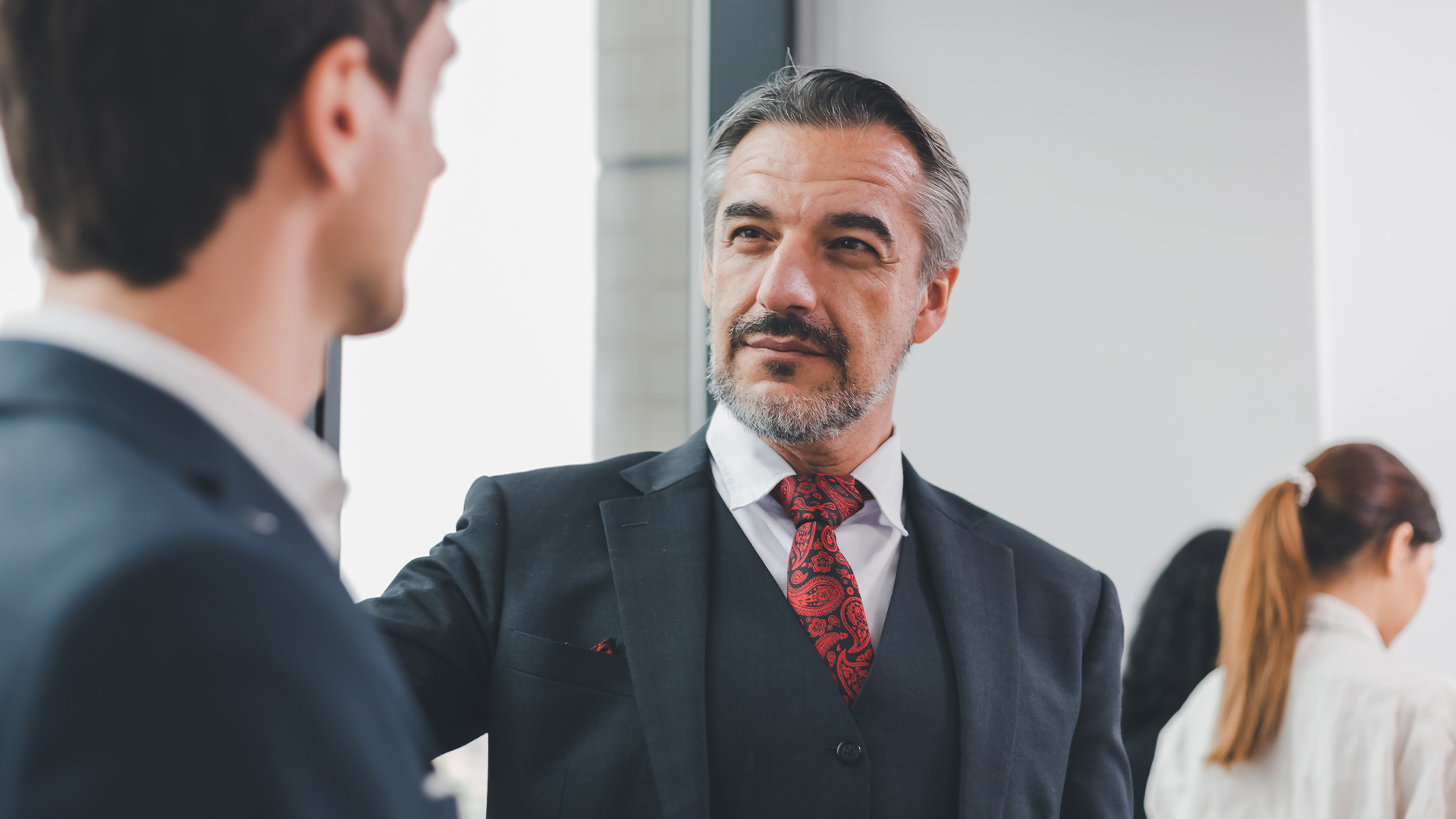 Two Caucasian businessmen wearing a formal suit, looking at each other eyes with pleasure smiling.